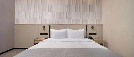 Une chambre d’hôtel moderne avec un grand lit, deux tables de chevet, un panneau lumineux fixé au mur et un téléphone sur chaque table.