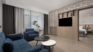 A modern hotel room with a sofa, two round tables, a TV, and a bed. - Wanda Yuehua Hotel Tangshan North (Tangshan)