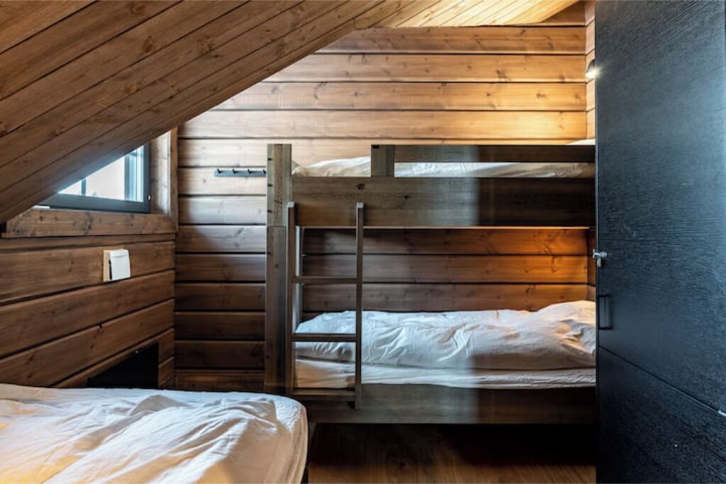 A dormitory room with wooden walls, a bunk bed, and a window.