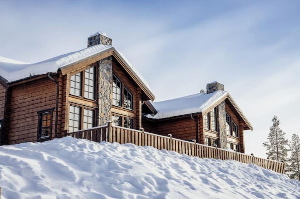 A large log cabin with a stone facade and multiple chimneys, surrounded by snow.