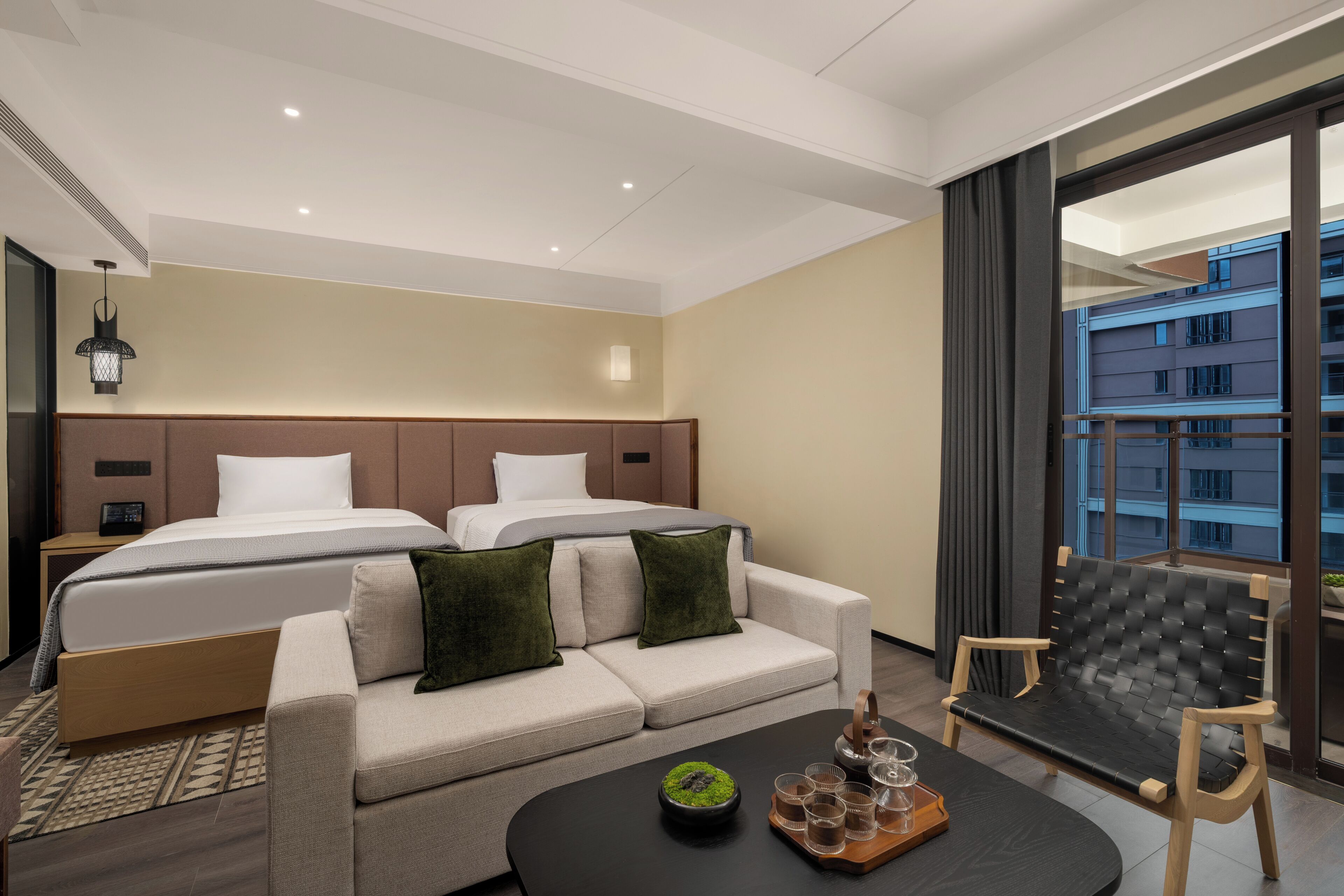 A hotel room with a bed, two sofas, a coffee table, and a balcony with a view of buildings.