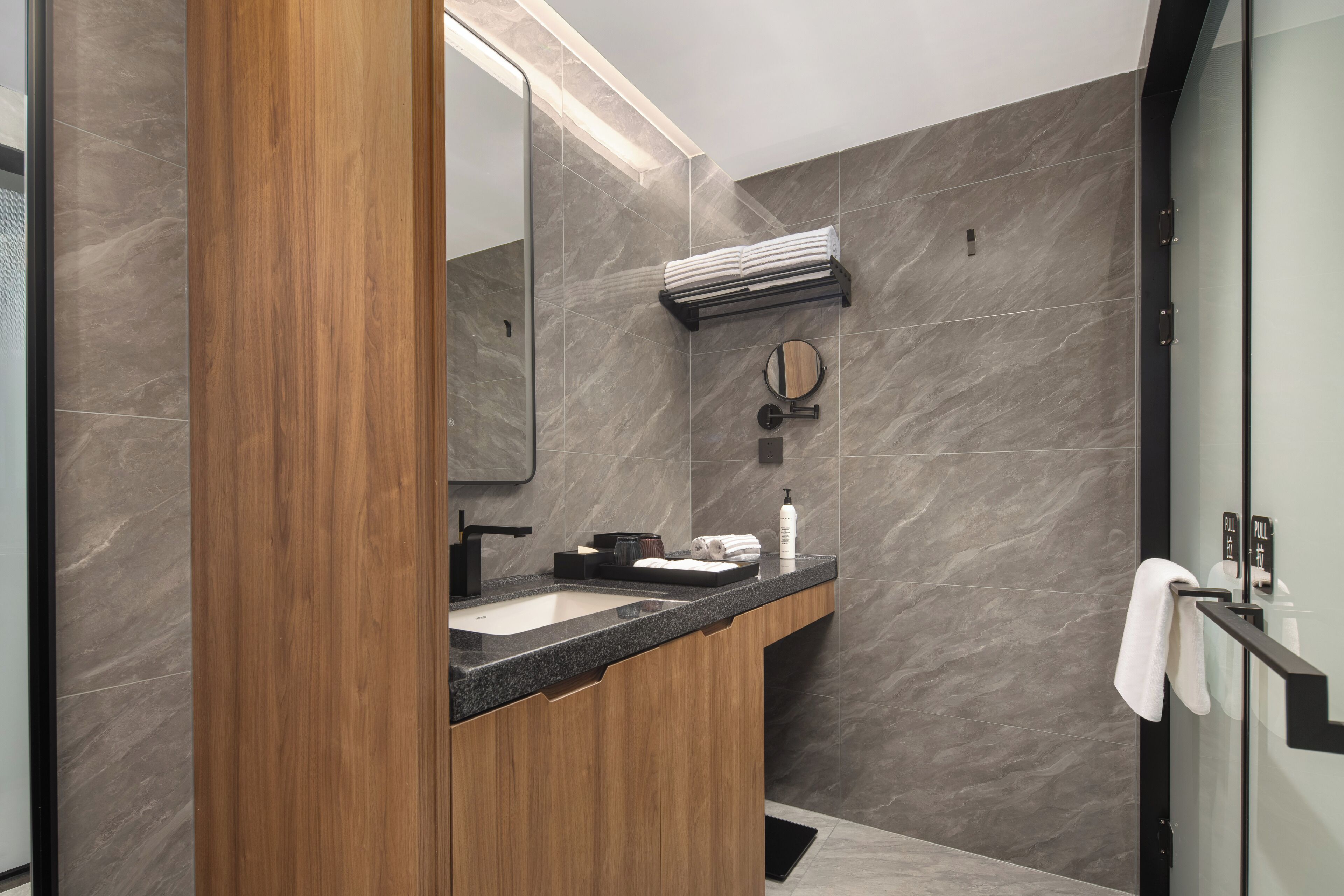A modern bathroom with a wooden vanity, a sink, a mirror, and a towel rack.