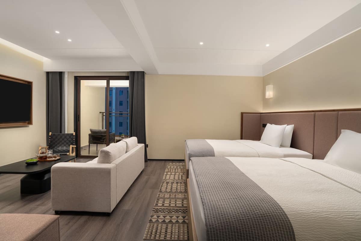 Een hotelkamer met twee bedden, een bank, een eettafel en uitzicht op de stad.