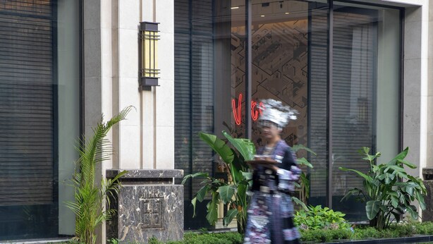 Un edificio moderno con ventanas amplias, una fuente reflectante y una persona caminando al frente.