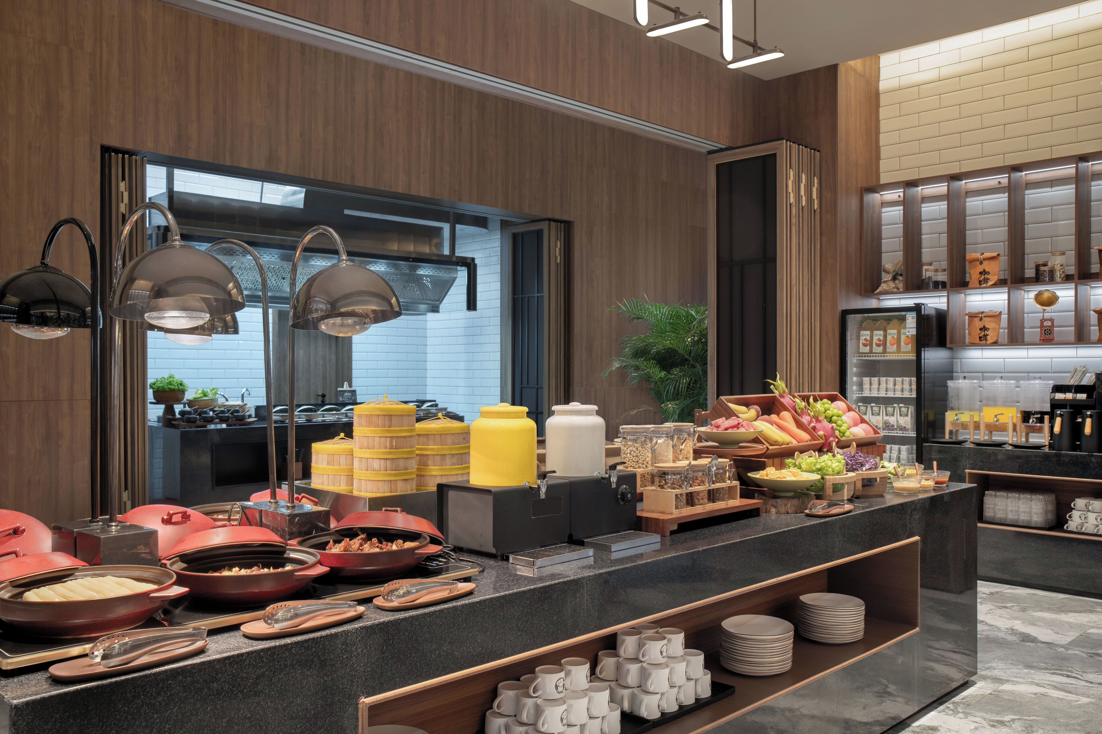 A buffet area with various food containers, a coffee station, and a refrigerator.