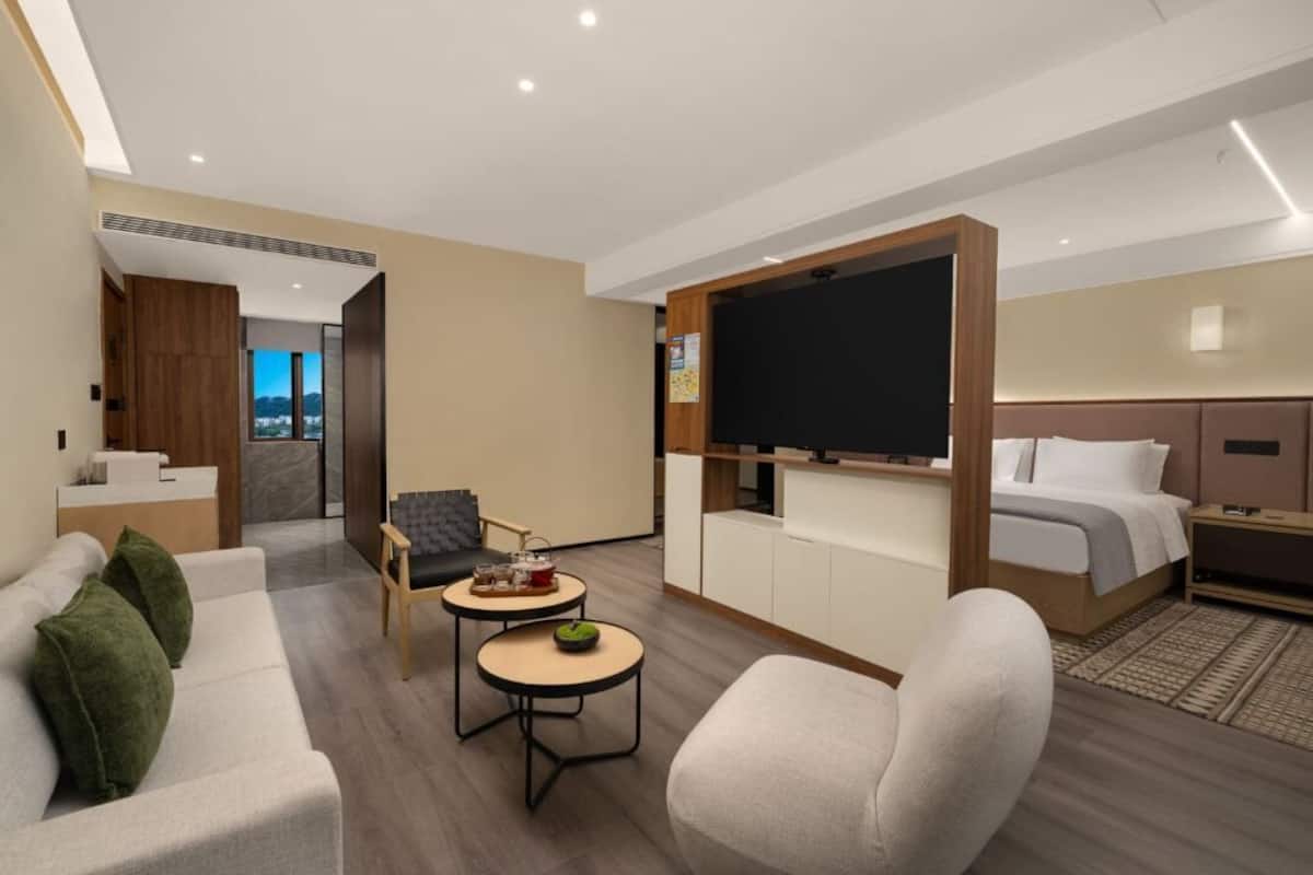 Een moderne hotelkamer met een bank, fauteuil, klein rond tafeltje en een bed met hoofdeinde.