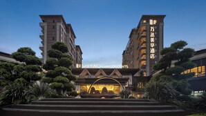 Una entrada de hotel moderna con un letrero destacado, rodeada de follaje cuidado y un cielo despejado.