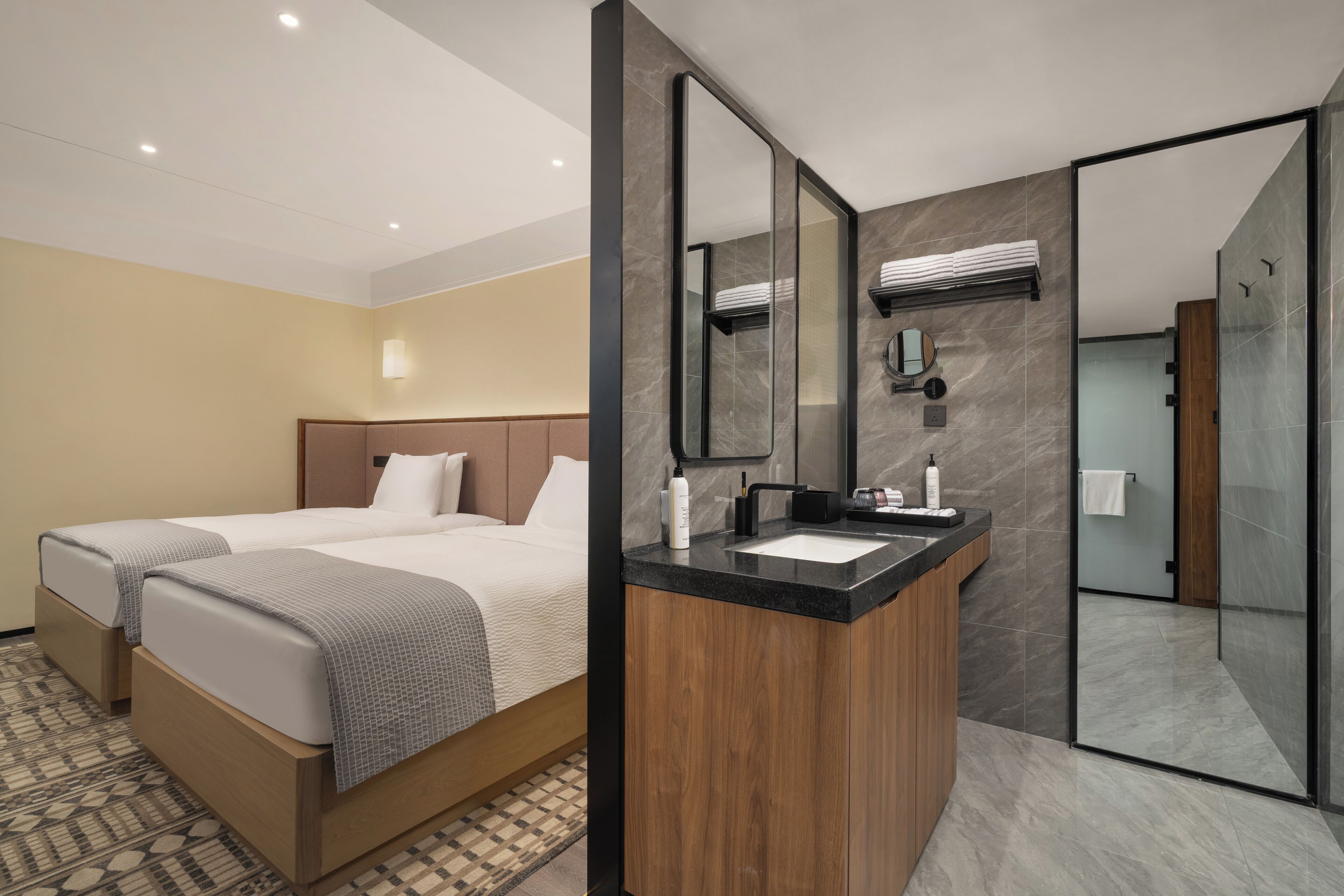 Habitación de hotel con dos camas, un tocador de madera, un espejo grande y zona de ducha.