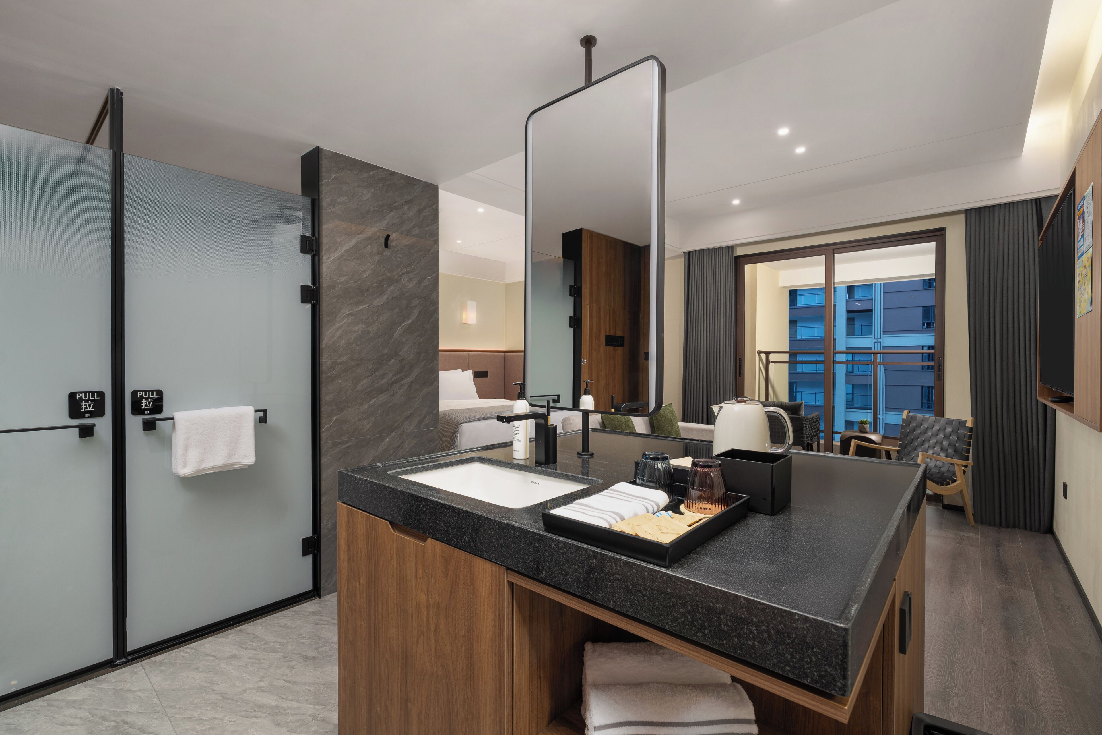 A modern bathroom with a glass shower enclosure, a large mirror, a sink with toiletries, and a view of a balcony.