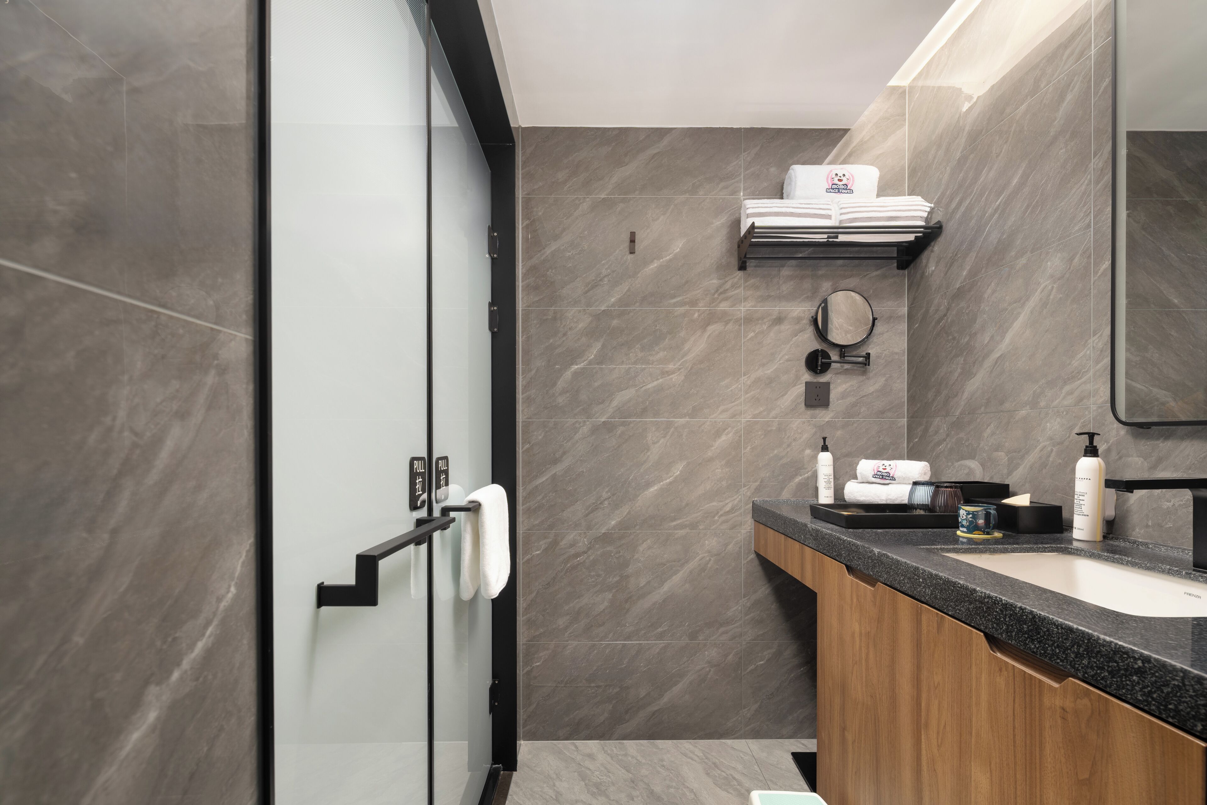 A modern bathroom with a glass shower door, a wooden vanity, and a large mirror.