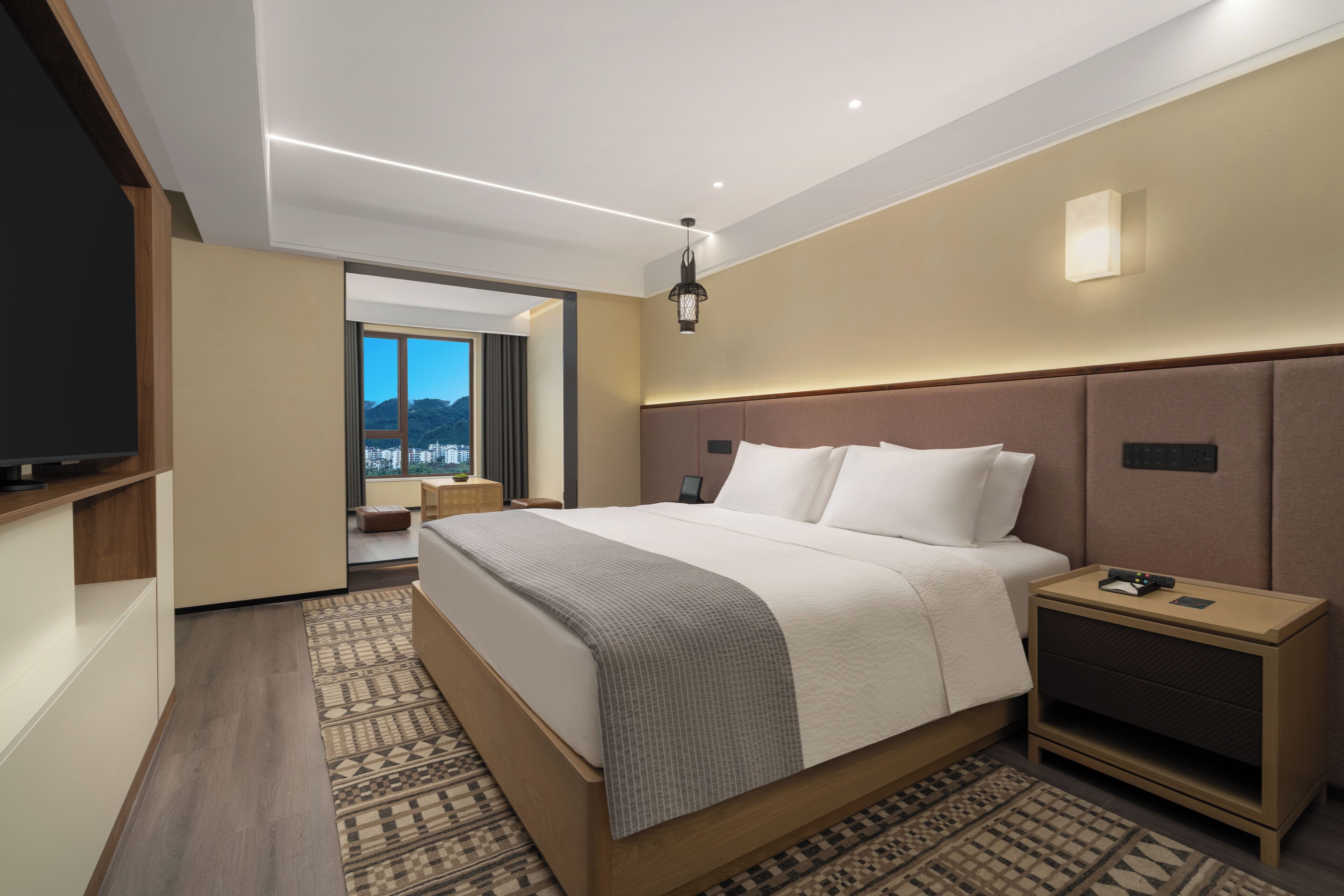 Habitación de hotel moderna con una cama grande, mesitas de noche, televisión y vistas a la ciudad.