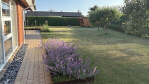 A garden with a paved walkway, a wooden structure, and a tree. - Lovely holiday home near beach and nature (Karrebæksminde)