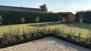 A paved patio area with a hedge and garden beds. - Lovely holiday home near beach and nature (Karrebæksminde)