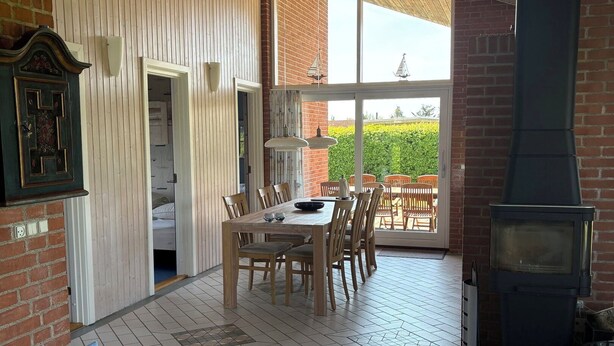 A spacious room with a wooden ceiling, a dining area with a table and chairs, a sofa, and a fireplace. - Lovely holiday home near beach and nature (Karrebæksminde)