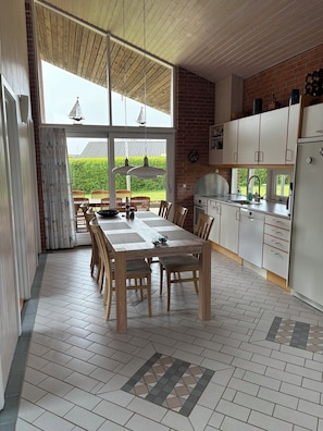 A modern kitchen with a dining area, large windows, and a view of the outdoors.