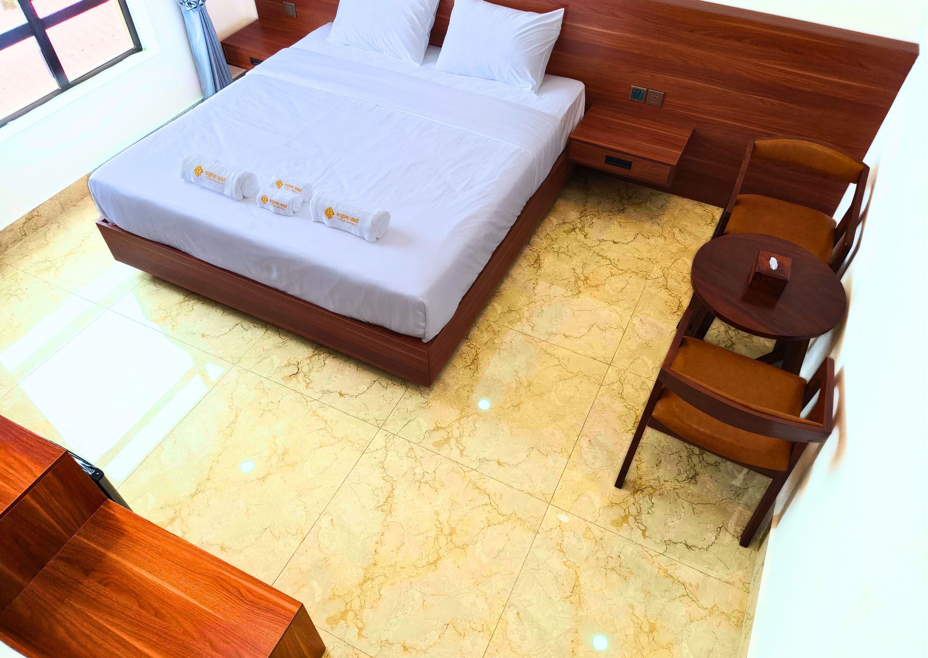 A hotel room with a large bed, a wooden nightstand, a small round table, and a chair.