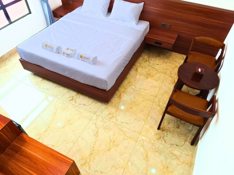 Una habitación de hotel con una cama grande, una mesita de noche de madera, una pequeña mesa redonda y una silla.
