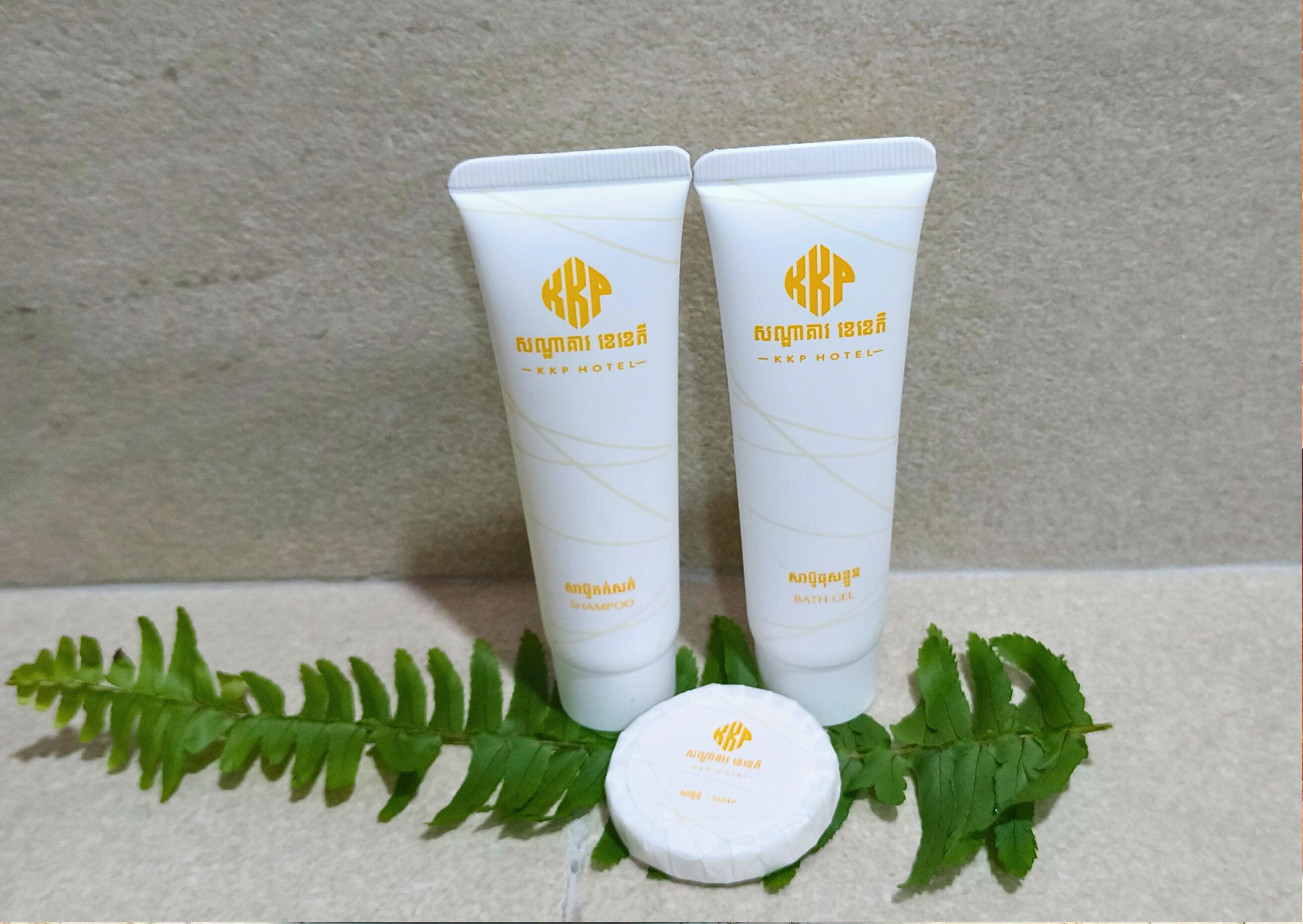 Two white tubes with yellow logos and text, a white round container, and green leaves.