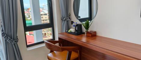 A hotel room with a wooden desk, a chair, a large mirror, and a window with curtains.