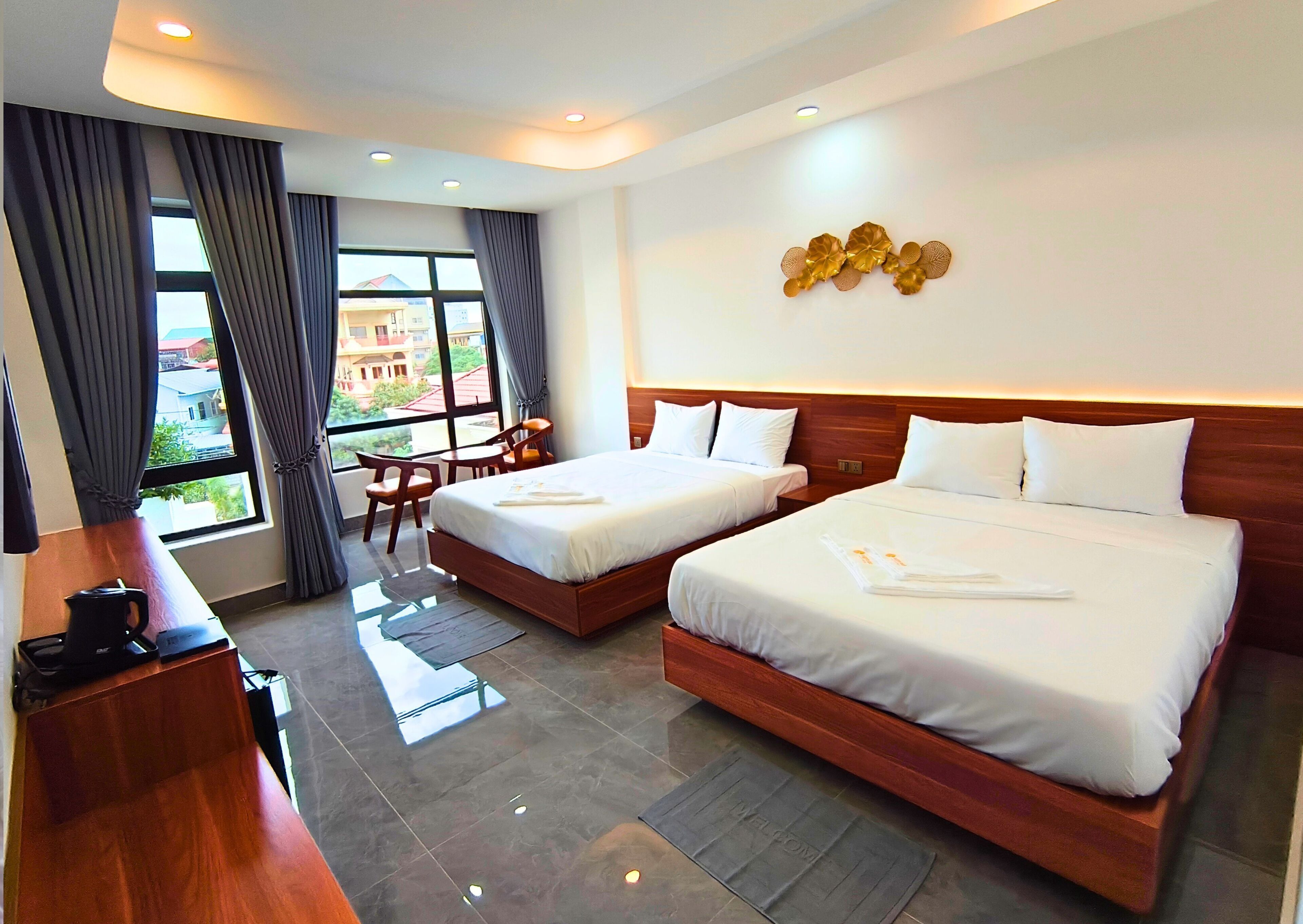 A hotel room with two beds, a desk, a chair, and a view of buildings outside.
