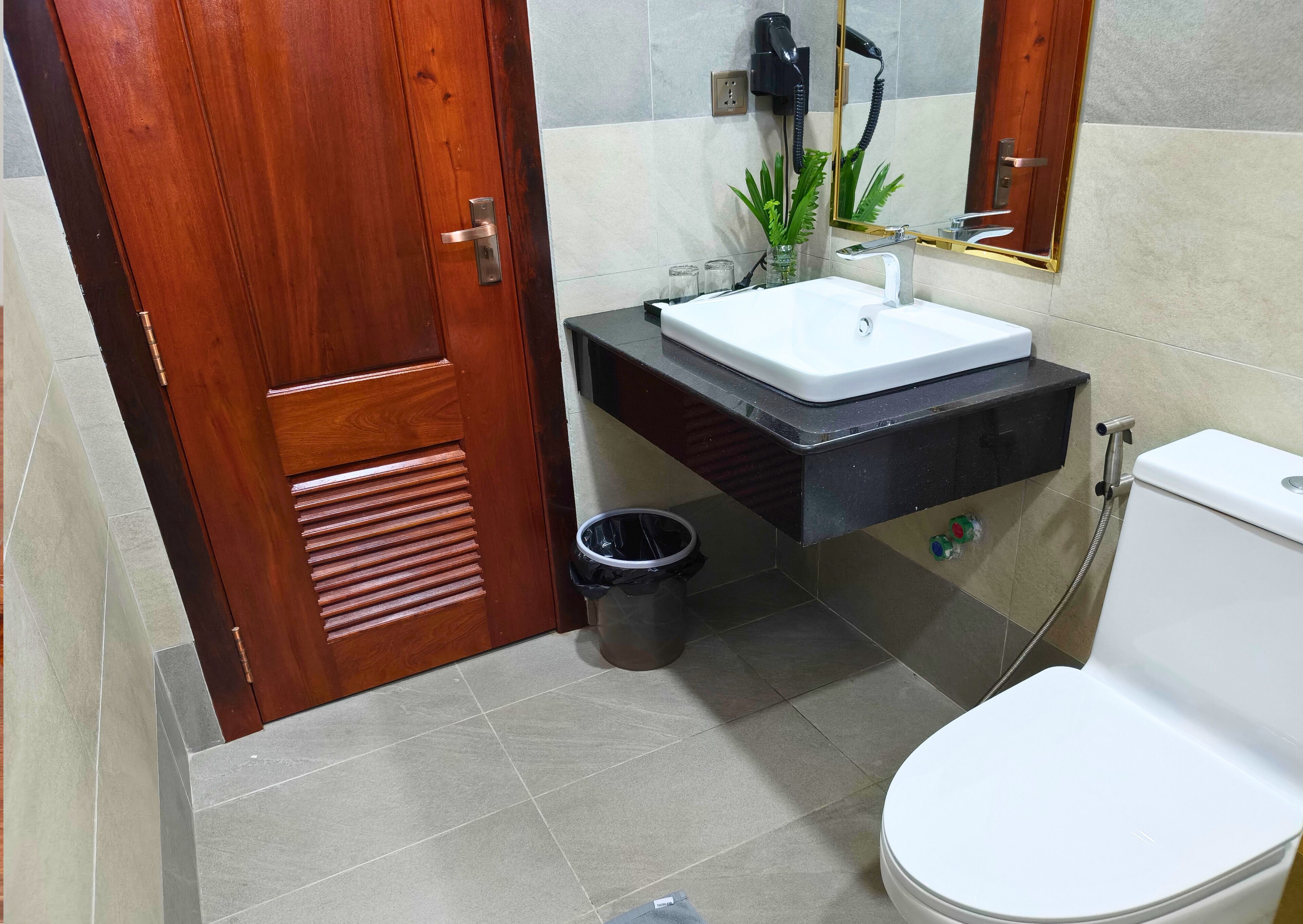 A bathroom with a wooden door, a white sink, a black vanity, a toilet, and a mirror.