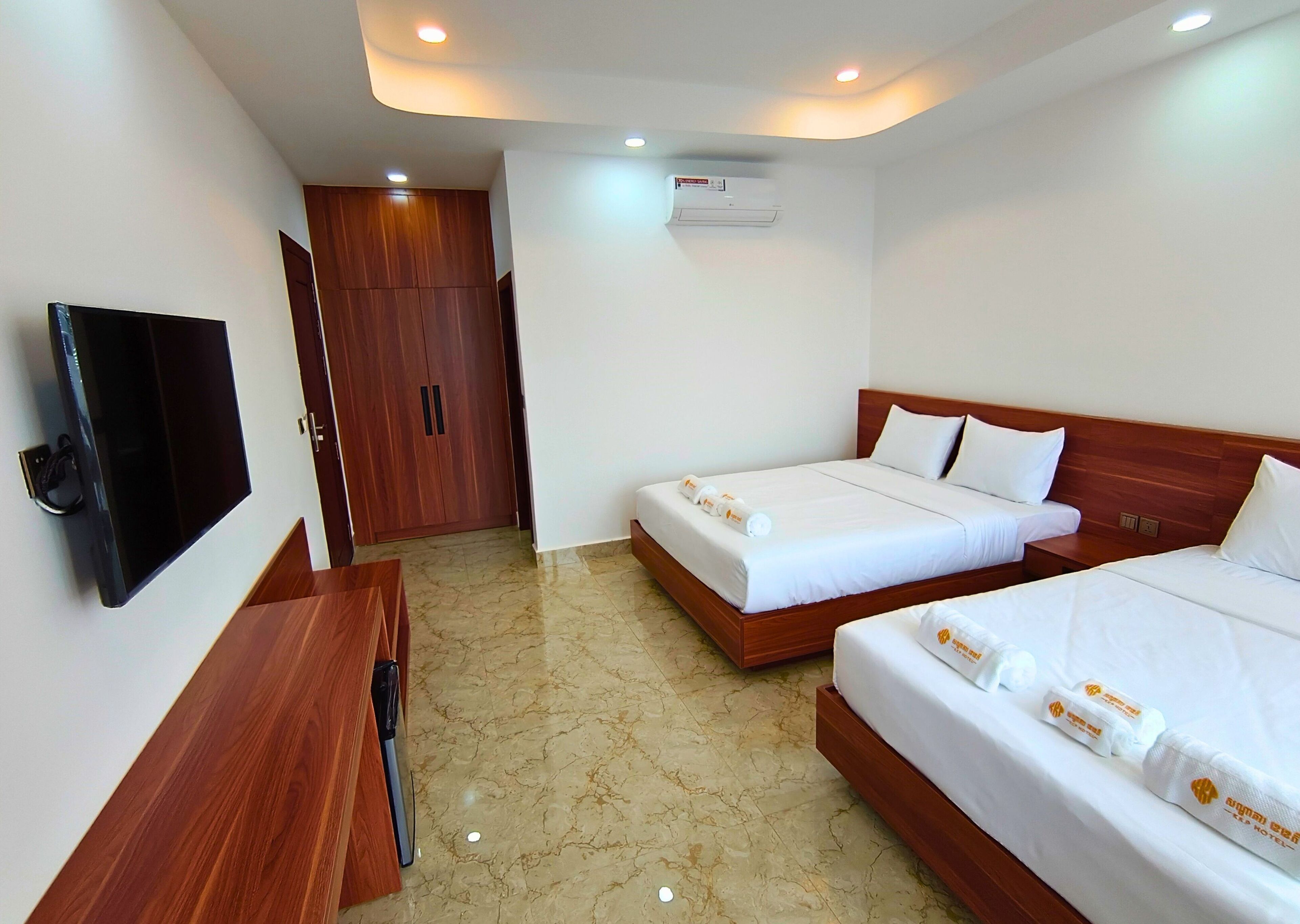 A hotel room with two beds, a TV, a wooden wardrobe, and an air conditioning unit.