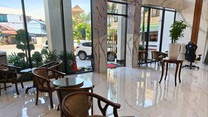 Un hall d’hôtel avec une cloison en verre, des chaises et des tables en bois.