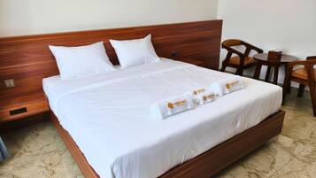 A neatly made bed with white linens and a towel with a logo, a wooden headboard, a wooden nightstand, and a small wooden table with chairs.