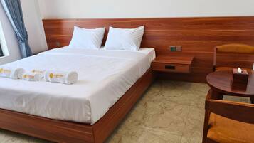 A hotel room with a wooden bed, white linens, a wooden nightstand, a round wooden table, and a chair.