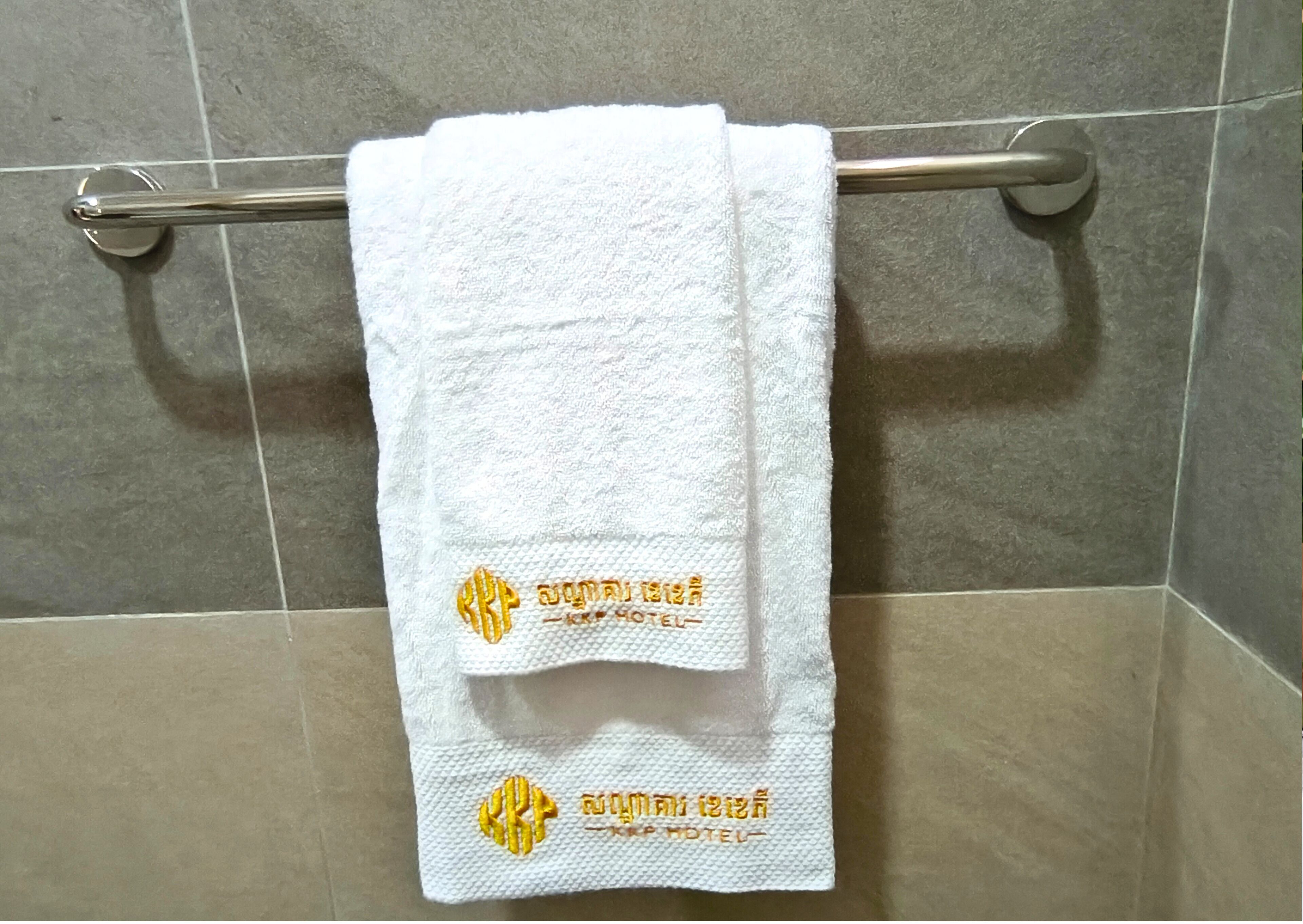 A white towel hanging on a metal towel rack in a tiled bathroom.