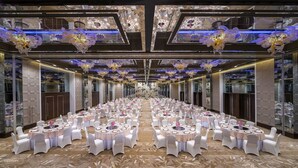 A banquet hall with round tables, white chairs, and floral centerpieces.