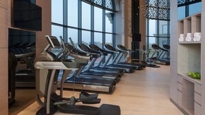 A row of treadmills in a gym with large windows and a wooden floor.