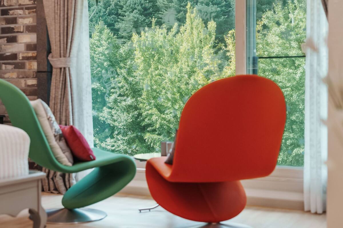 Une chambre moderne avec une grande fenêtre, un fauteuil vert et un fauteuil rouge.