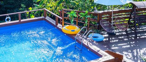 A wooden deck with a swimming pool, lounge chairs, and a lifebuoy.
