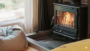 A cozy room with a wood-burning stove, a cushioned bench, and a view through a window. - Gapyeong Pinenut Pension (Gapyeong)
