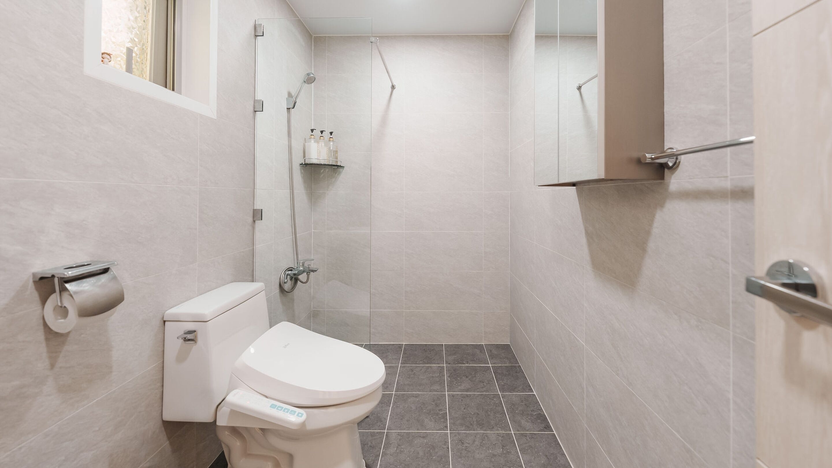 Un baño pequeño y moderno con inodoro, ducha y dispensador de papel higiénico.