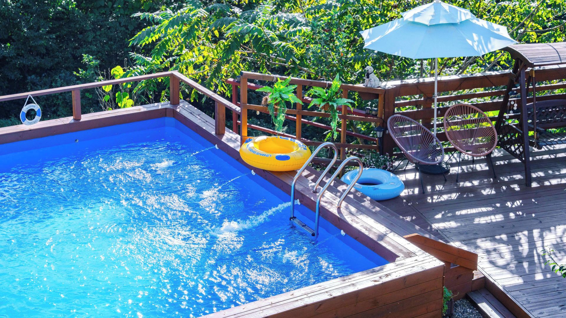 A wooden deck with a swimming pool, inflatable rings, and outdoor furniture.