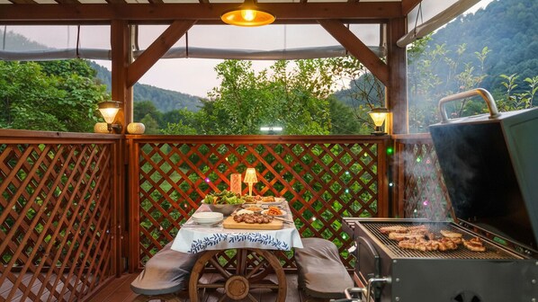 An outdoor patio with a grill, a table set for a meal, and a view of a forested area. - Gapyeong Pinenut Pension (Gapyeong)