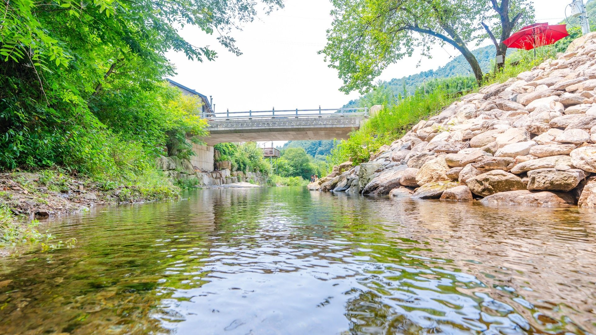 A river with a stone wall on one side and a bridge in the background.