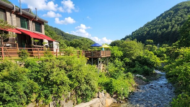 A riverside hotel with a deck overlooking the water, surrounded by lush greenery and hills. - Gapyeong Pinenut Pension (Gapyeong)