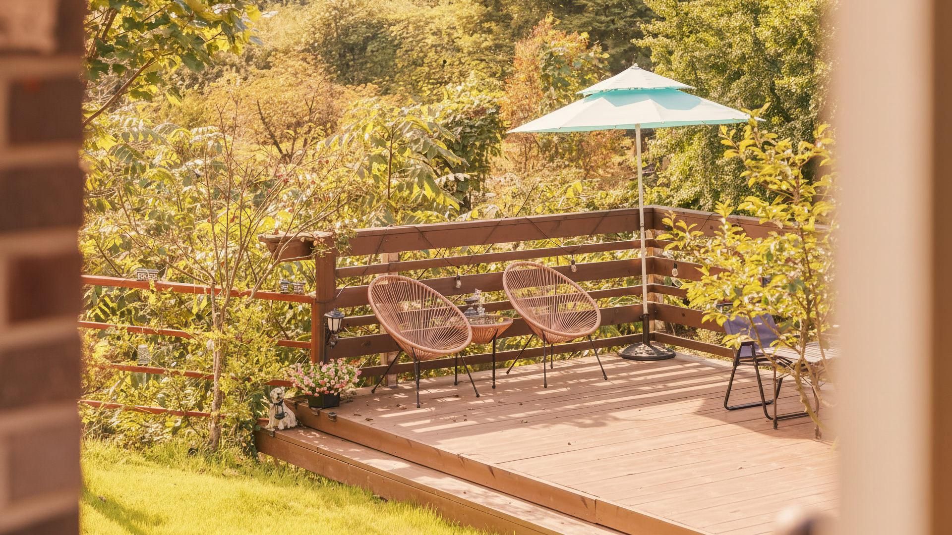 Eine Holzterrasse mit zwei Korbstühlen und einem Tisch, umgeben von Grünpflanzen.