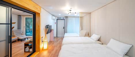 A modern hotel room with two beds, a wooden floor, a sliding glass door leading to a living area, and a ceiling fan.