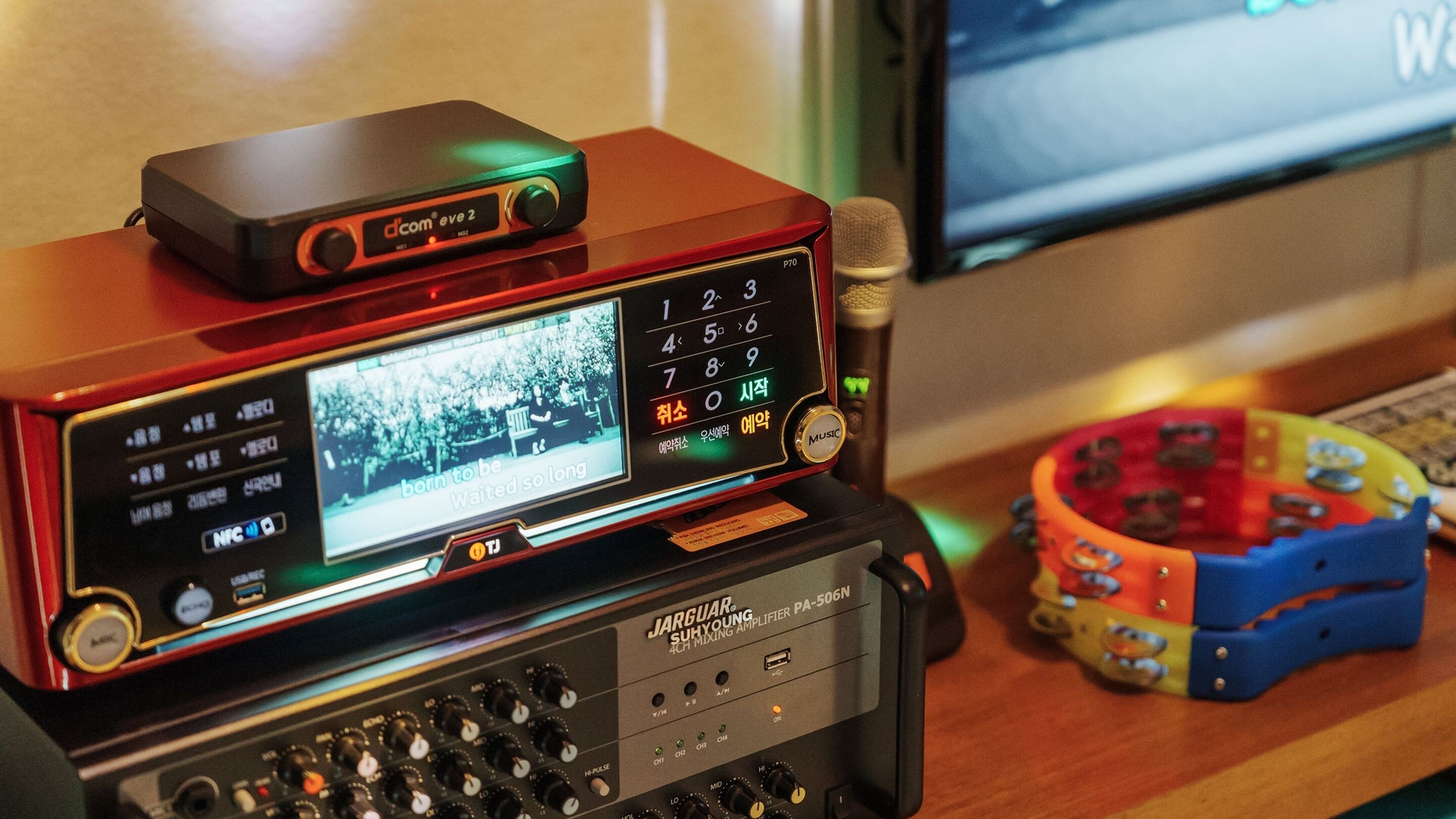 A JAGUAR SUHYOUNG 4CH MIXING AMPLIFIER PA-506N on a desk with a dcom eve 2 device, a microphone, and a colorful toy ring.