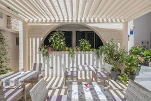 Eine Terrasse im Freien mit einer Pergola, einer Sitzgelegenheit und Kübelpflanzen.