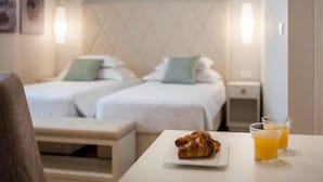 Ein Hotelzimmer mit zwei Betten, einem Nachttisch mit einem Croissant und zwei Gläsern Orangensaft, sowie einer wandmontierten Lampe.