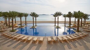 A poolside area with lounge chairs and palm trees, overlooking a beach and the sea.