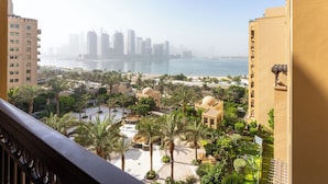 A view from a balcony overlooking a landscaped area with palm trees, a water body, and a distant city skyline.