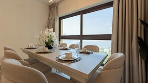A dining area with a table set for six, a vase of white flowers, and a view of the sea through large windows.