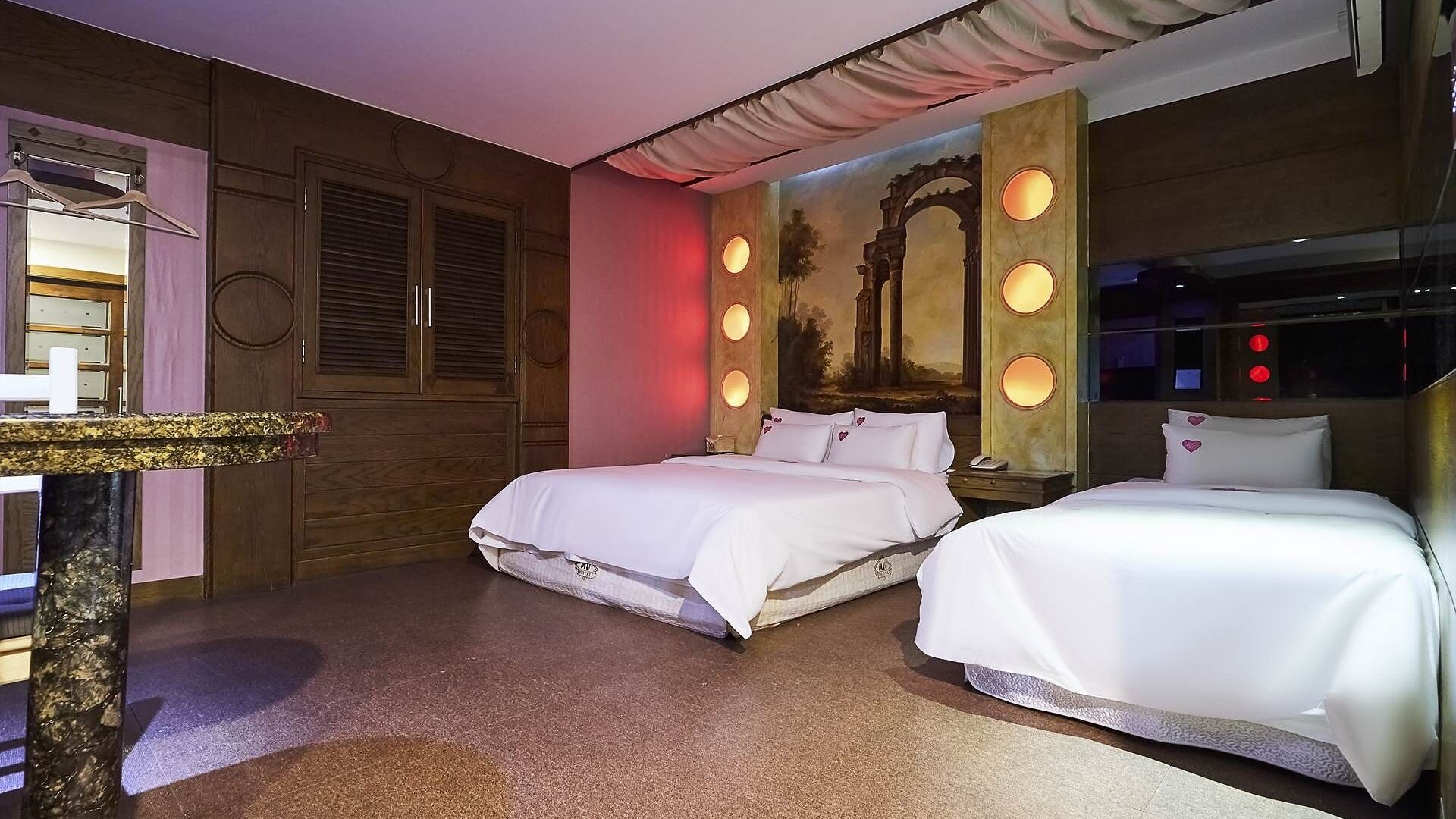 A hotel room with two beds, a vanity with a mirror, and a mural on the wall.
