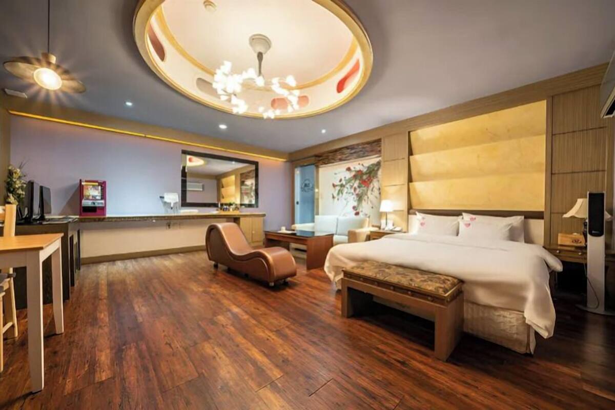 A hotel room with a large bed, a desk, a chair, a small table, and a ceiling light fixture.